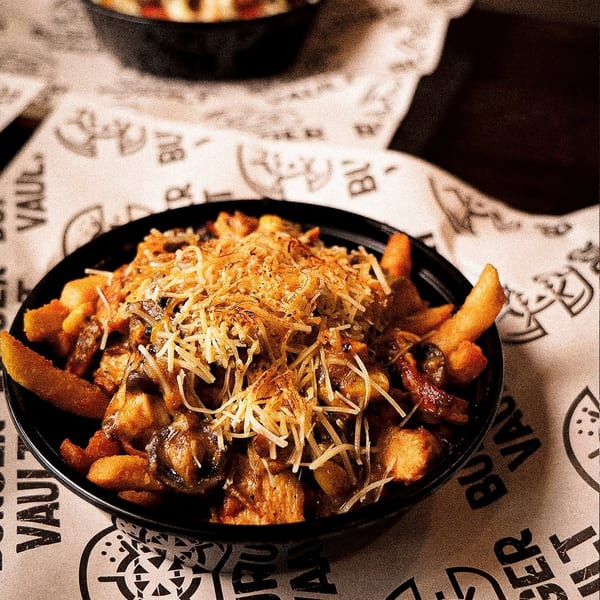 A black bowl of loaded fries topped with shredded cheese and mushrooms on branded paper.