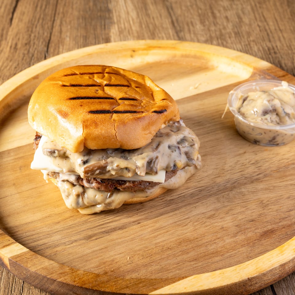 A mushroom Swiss burger with a side of mushroom sauce on a wooden plate.