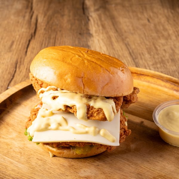 Double crispy chicken burger with cheese and sauce on a wooden board, with a side of dipping sauce.