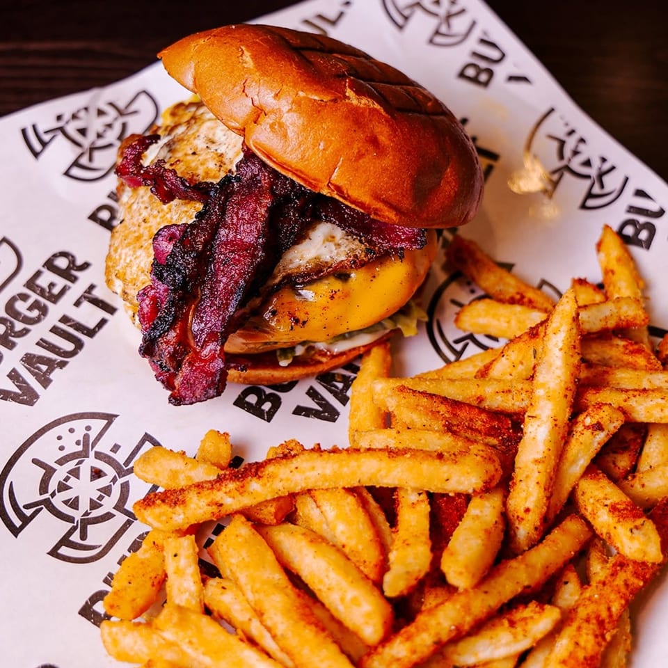 Bacon and egg burger on a brioche bun, served with seasoned fries on branded paper.