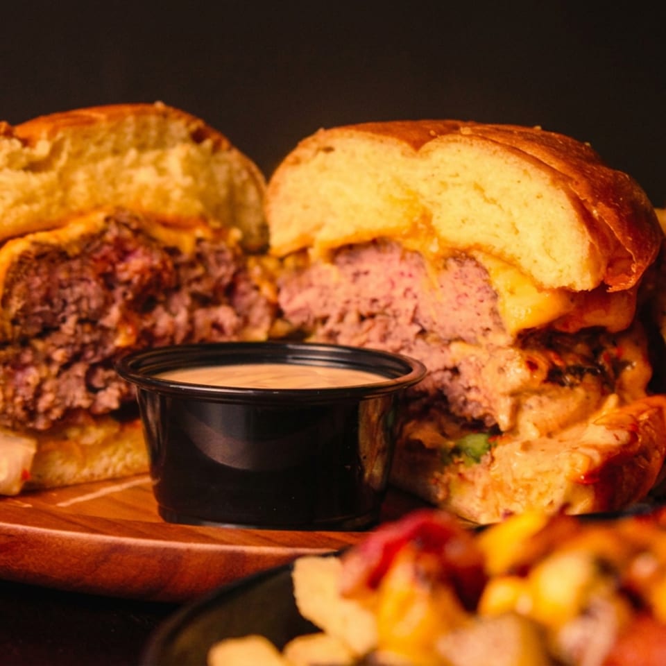 Juicy burger cut in half, revealing patty and melted cheese, served with fries and dipping sauce.