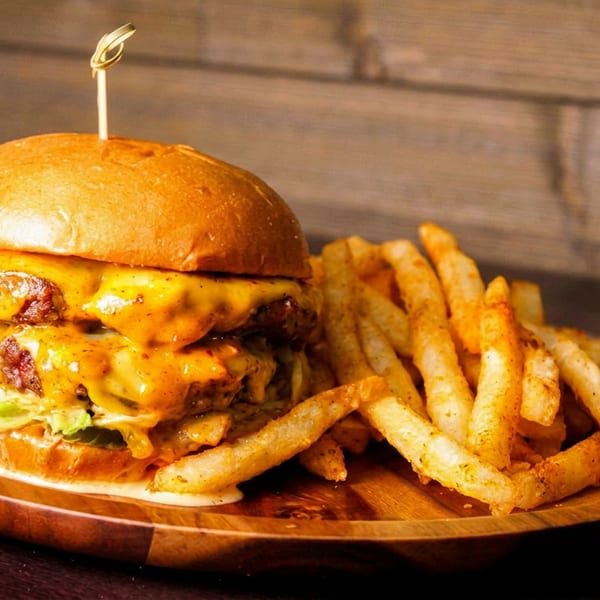 Juicy double cheeseburger with melted cheese and a side of seasoned fries on a wooden plate.