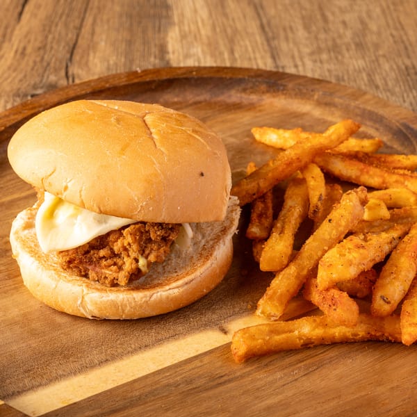A chicken burger with cheese and a side of seasoned fries on a wooden plate.