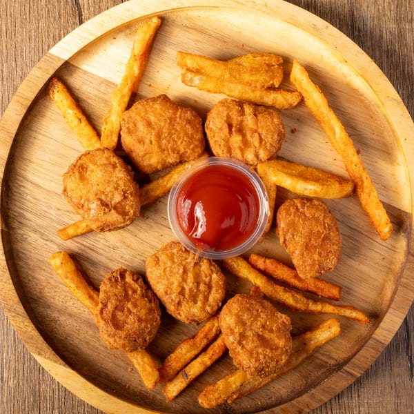 Golden chicken nuggets and french fries with a side of ketchup on a wooden platter.