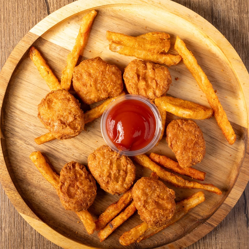 Golden chicken nuggets and french fries with a side of ketchup on a wooden platter.