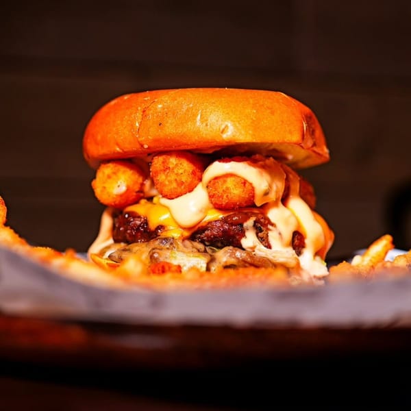 Close-up of a juicy burger topped with melted cheese, creamy sauce, and golden tater tots.