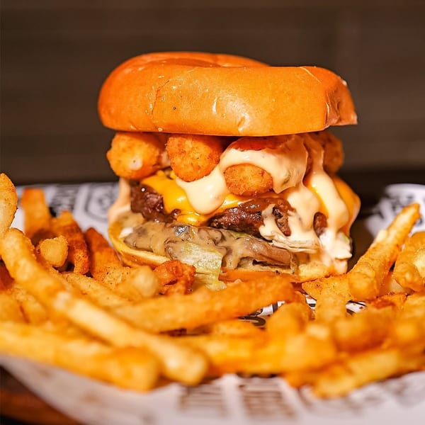 Loaded burger with tater tots, melted cheese, sauce, mushrooms, and a side of french fries.