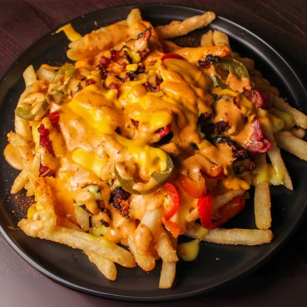 Loaded fries with melted cheese sauce, jalapeños, red peppers, and bacon on a black plate.