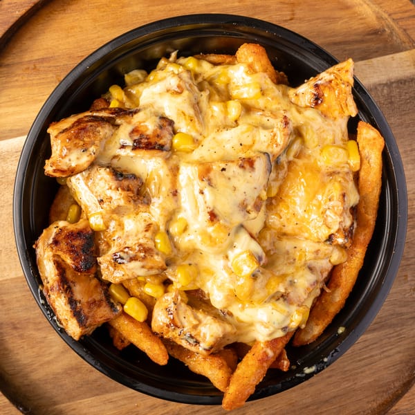 A black bowl filled with cheesy fries, grilled chicken, and corn on a wooden surface.